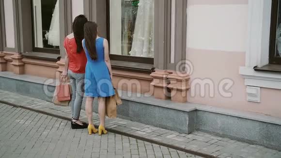 年轻的女孩朋友站在商店橱窗附近穿着婚纱讨论慢节奏视频的预览图