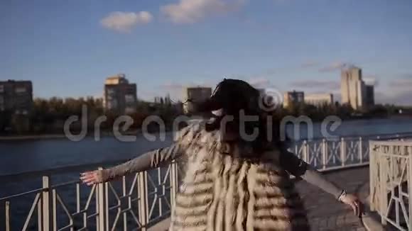 美丽的女孩在桥上快乐地旋转以城市为背景的河流柔和的阳光视频的预览图