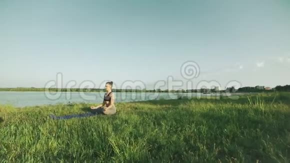 日出时处于莲花位置的漂亮女人早上在湖边做瑜伽的女孩视频的预览图