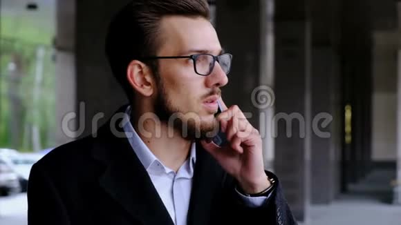 一位穿着经典服装戴眼镜的严肃商人站在办公室旁边的街道上回答视频的预览图