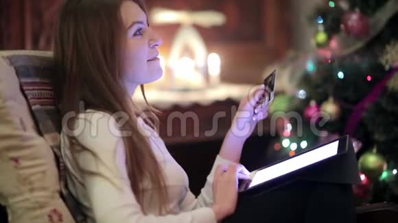 漂亮女孩坐在圣诞树旁的扶手椅上视频的预览图