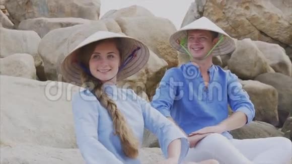 一个戴着越南帽子的男人和一个女孩坐在海滩上的岩石上摆出一个瑜伽的姿势冥想互相看着对方概念视频的预览图