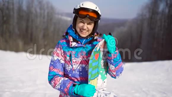 一个年轻快乐的女孩手里拿着一块滑雪板的肖像冬季晴天环山滑雪场A视频的预览图