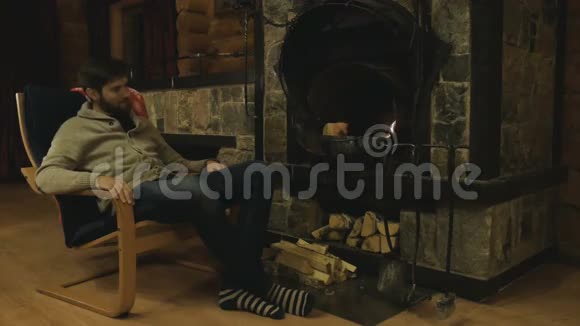 壁炉旁的扶手椅上的男人温暖冰冷的手温暖舒适的火壁炉里燃烧的火舒适视频的预览图
