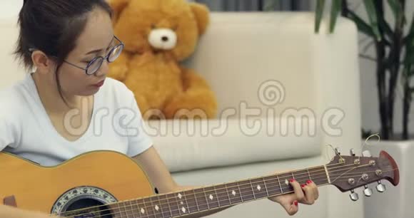 亚洲年轻女孩坐在长长的沙发椅上集中精力在家里学习弹吉他视频的预览图