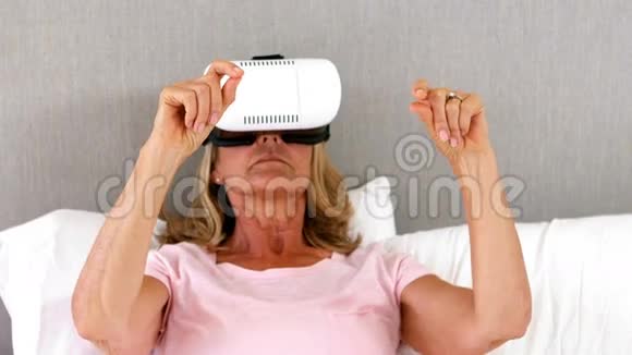 在卧室的床上使用虚拟现实耳机的高级妇女视频的预览图