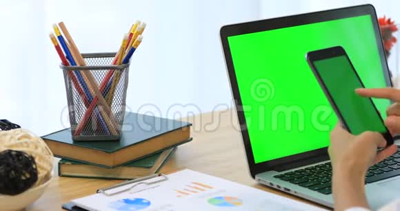 亚洲女人手拿手机带有绿色屏幕的桌子上的电话和笔记本电脑视频的预览图