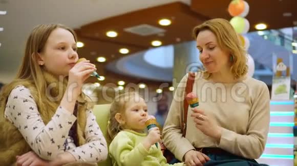 母亲带着女儿坐在绿色的小沙发上在购物中心的大厅里吃冰淇淋视频的预览图