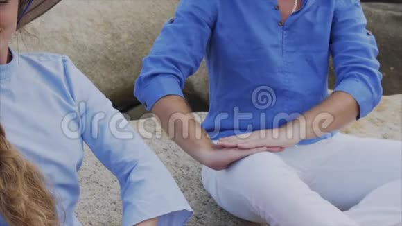 一个戴着越南帽子的男人和一个女孩坐在海滩上的岩石上摆出一个瑜伽的姿势冥想互相看着对方概念视频的预览图