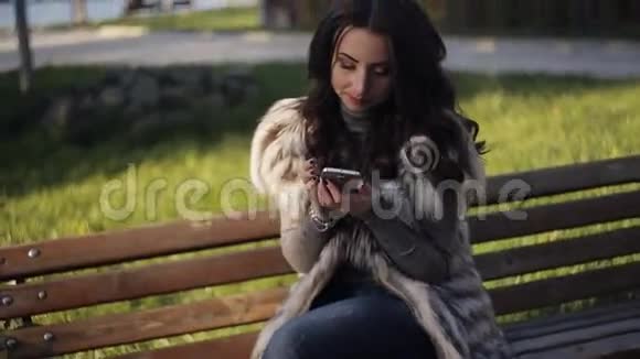 美丽的女孩在公园长椅上写短信电话视频的预览图