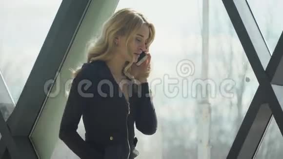 穿着黑色衣服的金发女孩站在窗边打电话视频的预览图