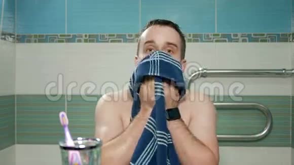 年轻有魅力的男人在酒店洗澡后用毛巾和手在浴室擦拭他的脸他看着视频的预览图