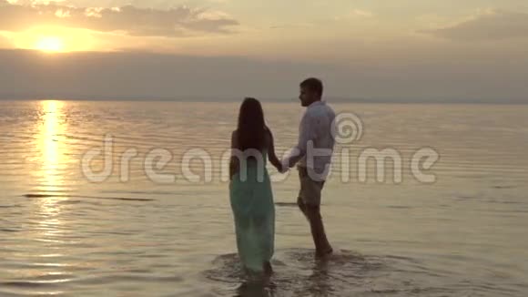 年轻快乐的男人在夕阳下的沙滩上接女友的爱情观视频的预览图