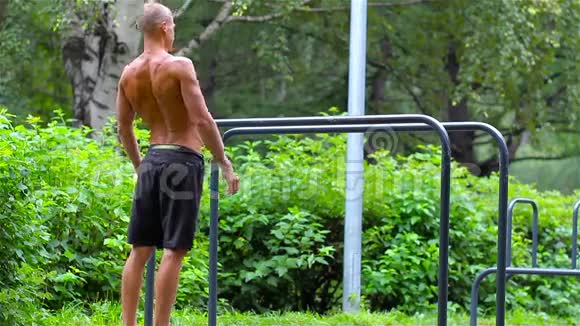 运动员在夏季树下的城市公园的酒吧里做运动前的热身运动视频的预览图