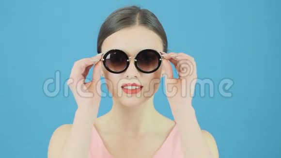 蓝色背景下不伦娜模特戴着时尚太阳镜和粉红色连衣裙的美画像完美女孩就是输视频的预览图