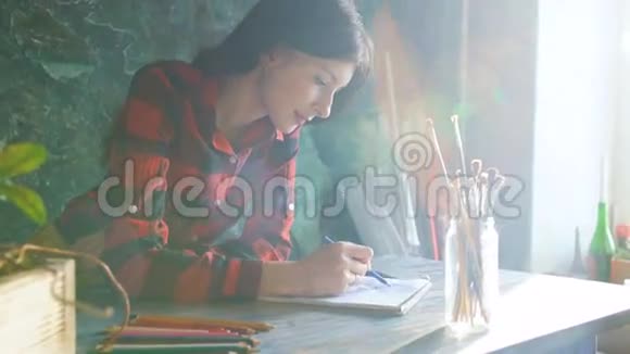 年轻的女艺术家用铅笔在纸笔记本上画明亮的太阳从窗户照进来视频的预览图