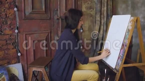 年轻的女画家用铅笔在画架画布上画画准备画画视频的预览图