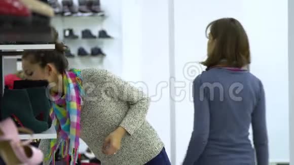 两个年轻漂亮的女孩在时装精品店里挑选鞋子女孩们聚精会神地看着鞋子检查它视频的预览图