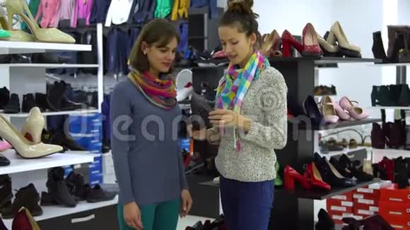 两个年轻漂亮的女孩在时装精品店里挑选鞋子女孩们聚精会神地看着鞋子检查它视频的预览图