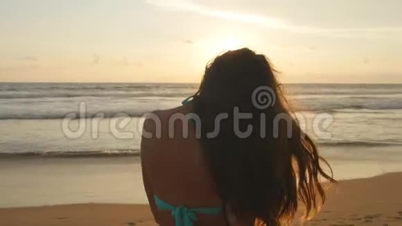 美丽的年轻女子穿着比基尼站在海边日落漂亮的女孩长发在海洋上摆姿势视频的预览图