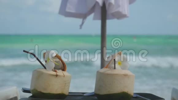 热带新鲜椰子鸡尾酒在海滩咖啡馆与绿松石海背景和变化的重点以海3840x2160视频的预览图