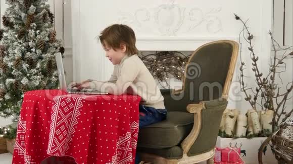 小男孩微笑着在圣诞树附近的笔记本电脑上给圣诞老人打信视频的预览图