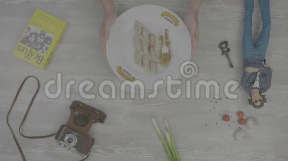 双手放一盘准备好的煎饼桌子上摆着一本书一台旧相机洋葱大蒜和玩具镜头视频的预览图