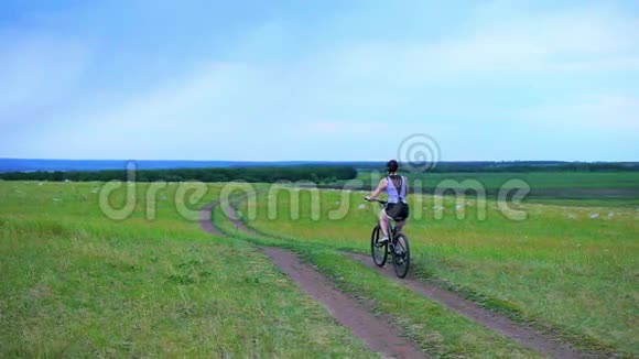 在炎热的夏日日落时年轻女子穿着一件连衣裙在田野里骑着老式自行车概念照片女视频的预览图