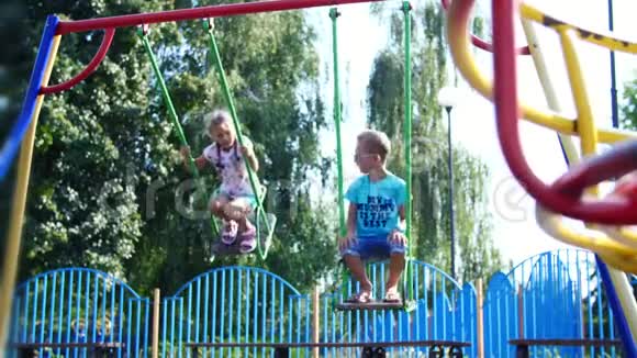 快乐的孩子们一个女孩和一个七岁的男孩骑在秋千上在炎热的夏天慢动作快乐的童年视频的预览图