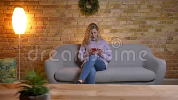 一位成年白种人金发女性在舒适的室内沙发上发短信时的特写镜头视频的预览图