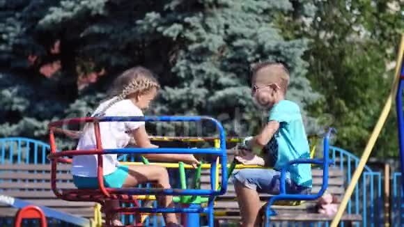 快乐的孩子们一个女孩和一个七岁的男孩骑在秋千上在炎热的夏天慢动作快乐的童年视频的预览图