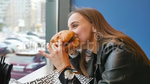 一个女孩特写的肖像手里拿着一个汉堡包一个年轻漂亮的女人在咖啡馆吃汉堡包食品快餐视频的预览图
