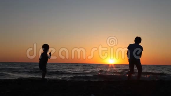 两个男孩在海滩上向海里扔石头的剪影视频的预览图