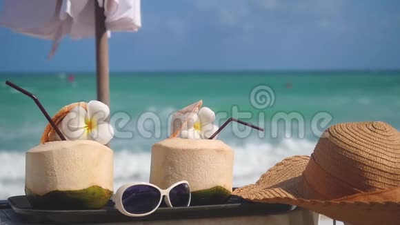热带新鲜的椰子鸡尾酒在海滩咖啡馆中装饰了花帽子雨伞和太阳镜并带来了变化视频的预览图