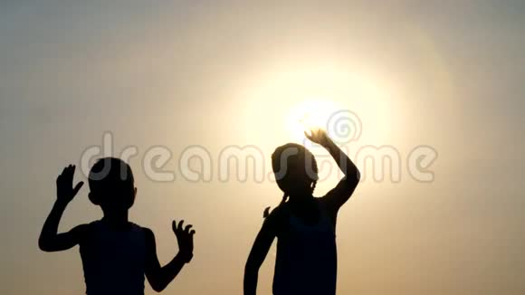 剪影儿童的身影男孩和女孩跳跃玩得开心跳舞在阳光的背景下拥抱视频的预览图