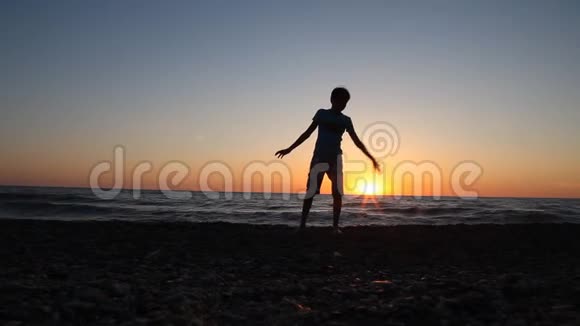 两个男孩在海滩上向海里扔石头的剪影视频的预览图