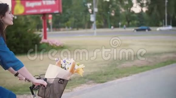 从侧面和背面看一个女孩骑着自行车花和法国面包在篮子里在城市慢莫稳定的镜头视频的预览图