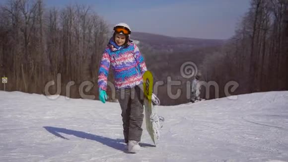 一个年轻快乐的女孩手里拿着一块滑雪板的肖像冬季晴天环山滑雪场A视频的预览图