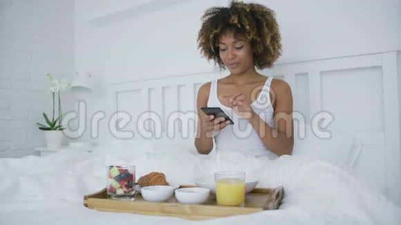 有智能手机的女人在床上吃饭视频的预览图