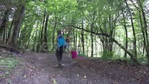 妈妈带着一个粉红色的背包在树林里牵着女儿的手健康的生活方式家庭在户外的树林里散步视频的预览图