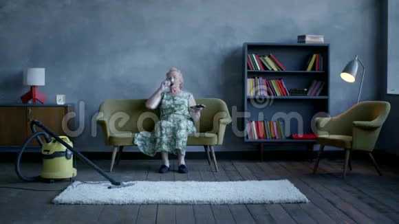 快乐的老妇人放弃了清洁坐下来放松喝了酒看了电视视频的预览图