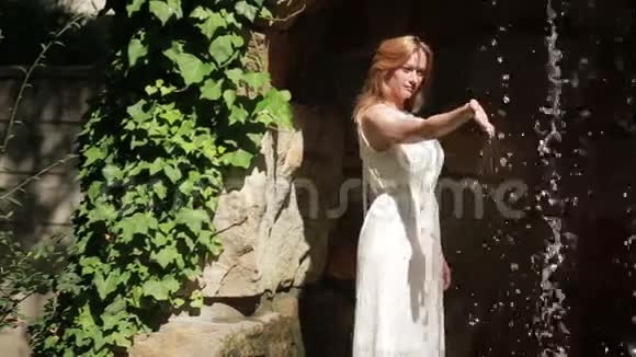 穿着白色连衣裙的女孩正在碰水它站在瀑布旁边视频的预览图