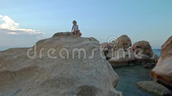 小女孩在海滩日落时爬上大岩顶视频的预览图