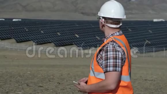 戴着头盔和背心的工程师在沙漠中的太阳能电池板项目上工作视频的预览图