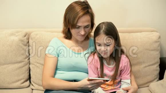 妈妈和女儿坐在沙发上看智能手机上的视频视频的预览图