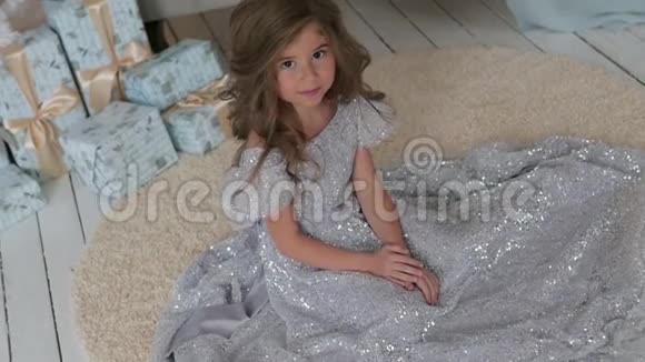 那个女孩坐在一件漂亮闪亮的连衣裙上圣诞节室内视频的预览图