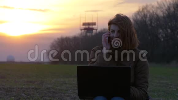 漂亮的红发女孩在通讯雷达附近使用笔记本电脑和智能手机视频的预览图