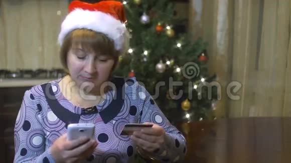 带圣诞帽的中年妇女通过信用卡从手机上购买视频的预览图