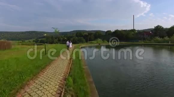 婚礼当天新娘和新郎沿着湖边散步的空中景色新婚夫妇穿着传统西装视频的预览图