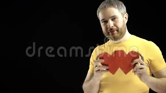 穿黄色T恤的开朗男人有两个红色的心形爱情浪漫约会关系概念黑色背景视频的预览图
